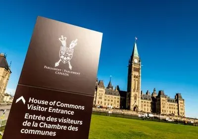 photograph of the canadian house of parliament against a blue sky.  a sign in the foreground indicates what the building is. 